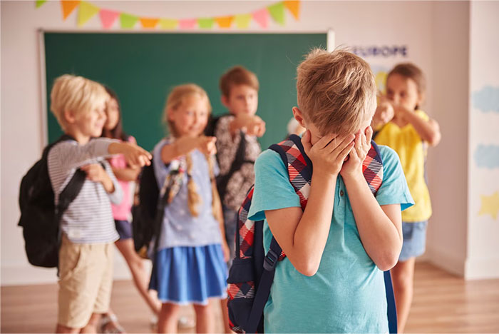 Child feeling upset during a school presentation, classmates pointing and laughing in the background.