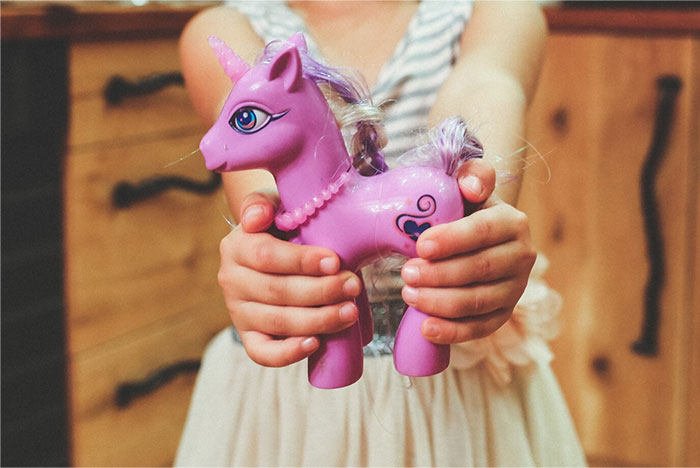 Child holding a pink toy unicorn, possibly used in a school presentation.