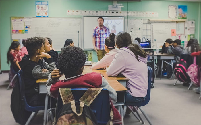 Students in a classroom watching a teacher, during a school presentation.