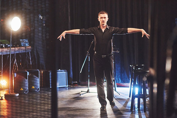 Man on stage with arms outstretched in a dramatic school presentation setting.