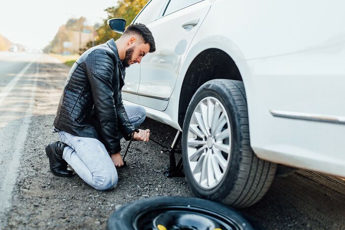 Man changing a flat tire on the roadside, experiencing an unexpected coincidence.