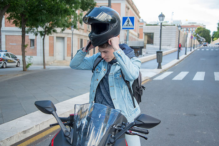 A person prepares to ride a motorcycle, putting on a helmet on a city street, focusing on employee's motorcycle.