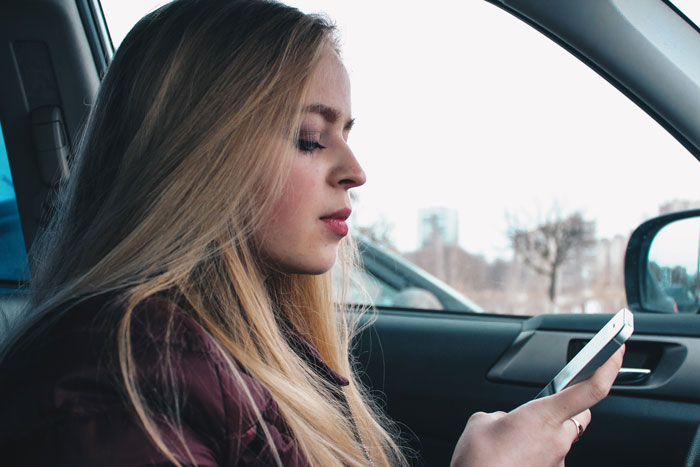 Woman wondering in a car, contemplating reasons her boyfriend won't let her visit his home, holding a phone.