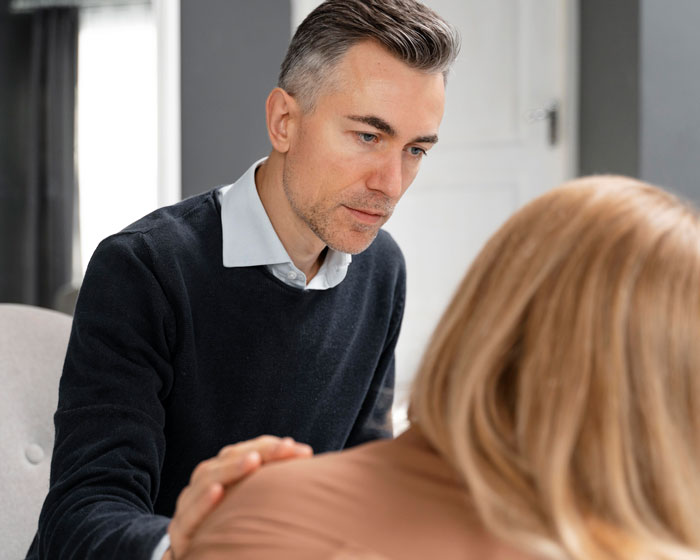 Man comforting a woman in a gray room, engaging in a thoughtful conversation about relationship concerns.