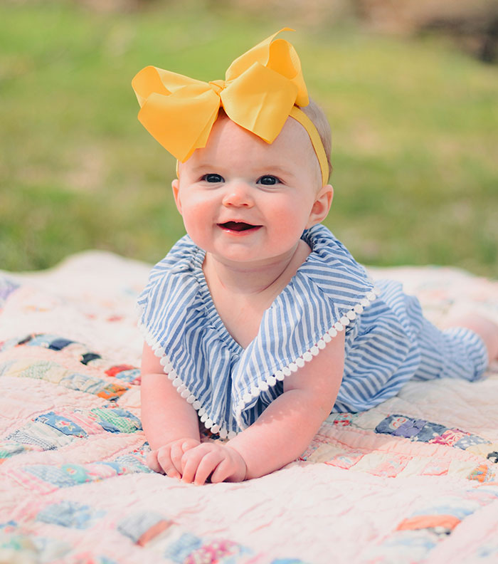 Baby with a yellow bow on a colorful quilt, related to child-free wedding controversy.