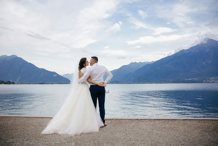 Bride and groom embracing by a lakeside during a brother's wedding engagement ceremony.