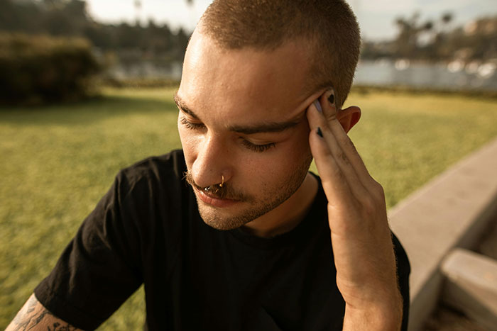 Man in a garden showing frustration, resting his head on his hand, dealing with unexpected wedding chores from family.