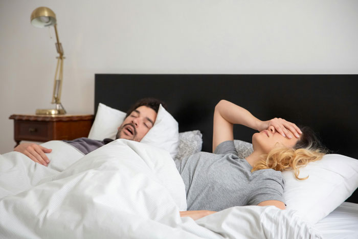 Family sleeping in hotel room with lamp and white bedding, unaware of smoke issue.