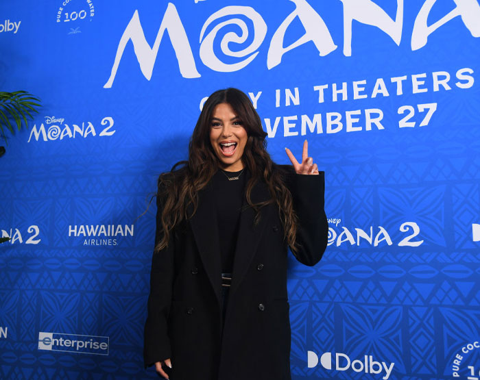 A person posing at a Moana 2 event, wearing a black coat, with SEO keyword: "The Cast Of Only Murders In The Building".