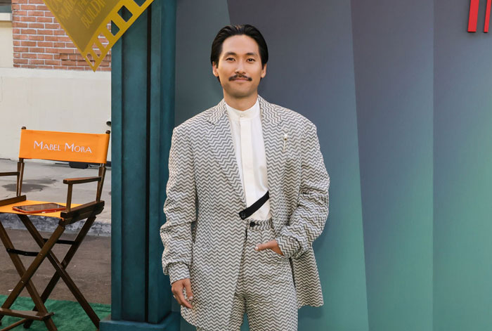 Person in a patterned suit standing beside a director's chair at an event for "Only Murders In The Building" Season 4.