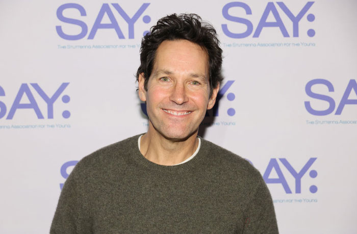 Actor at an event, smiling in front of a SAY: backdrop, representing the cast of "Only Murders in the Building."