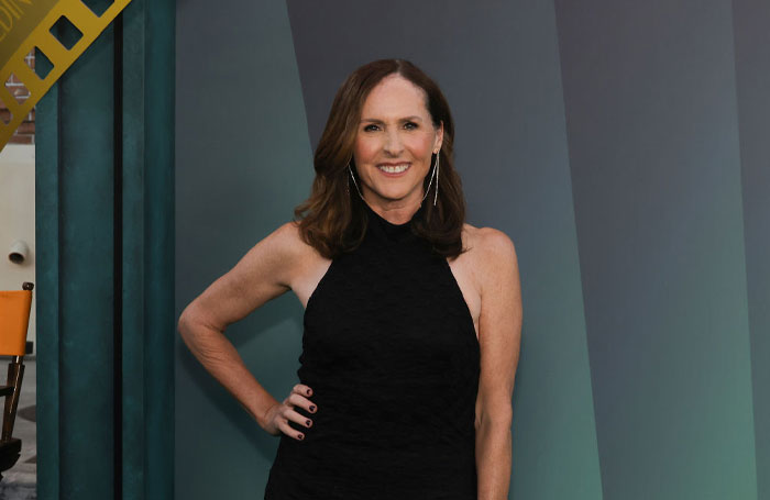 A smiling woman in a black dress at a "Only Murders in the Building" event, standing against a gradient background.