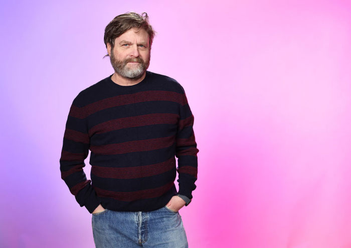 A man in a striped sweater poses against a pink background, representing hidden gems in season 4 of "Only Murders in the Building."