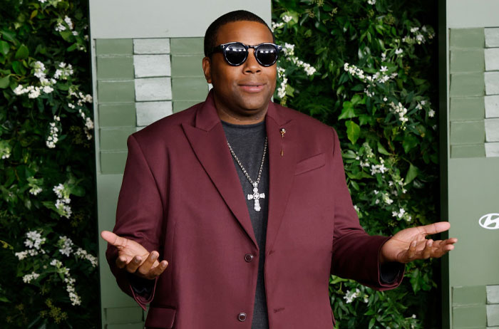 Person in sunglasses and maroon jacket at musical extravaganza event, posing with greenery background.