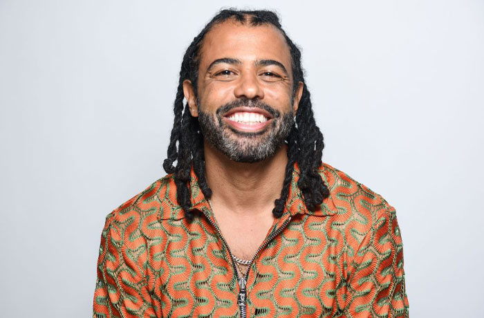 Smiling man with dreadlocks in a patterned shirt representing Trolls 3 cast.