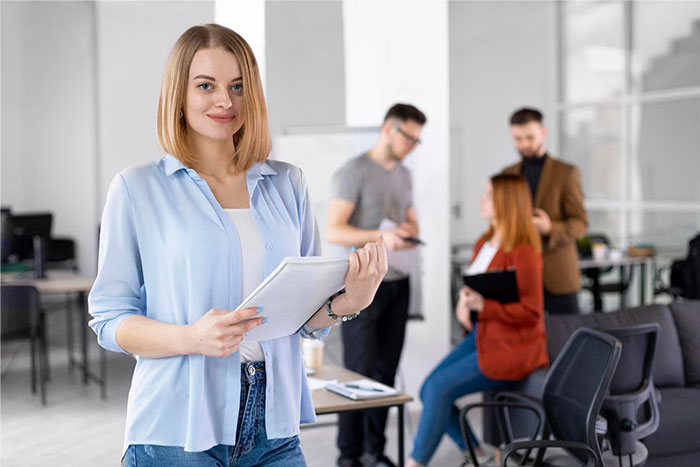 Smiling woman in office setting with colleagues; HR director experiencing stress in the background.