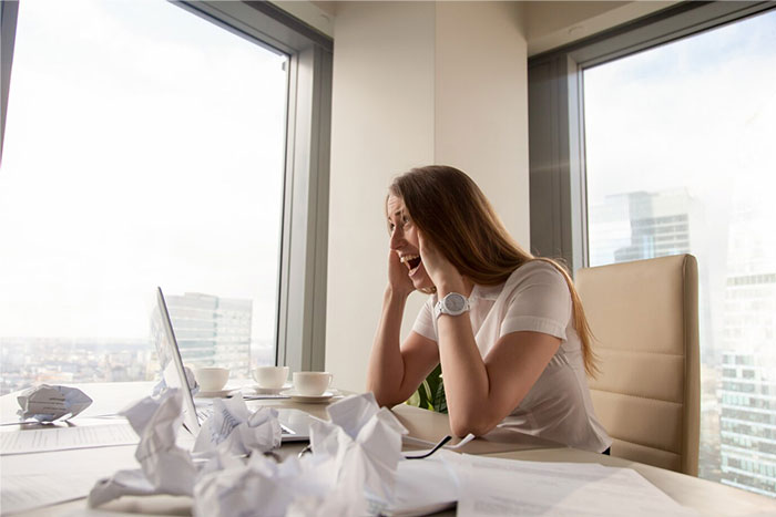 HR Director appearing stressed in an office, surrounded by crumpled papers, looking at a laptop.