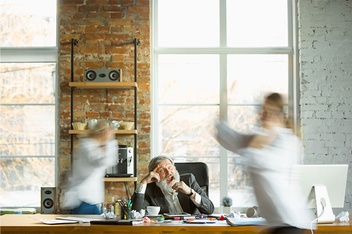 HR director stressed at desk as two colleagues rush past in a busy office setting.