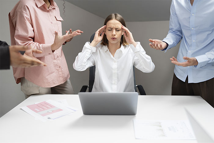 HR director stressed at desk, surrounded by colleagues, laptop open.