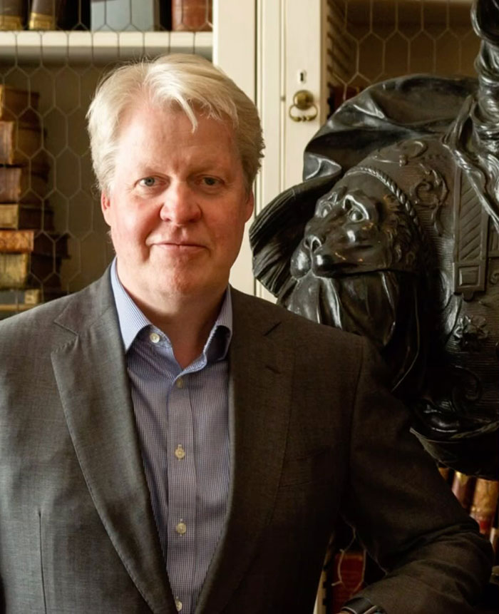 A man in a suit stands beside a statue in a library, related to the Earl-Spencer mistress controversy.