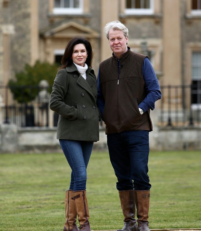 A man and woman standing outdoors, wearing casual outfits, in front of a historic building.