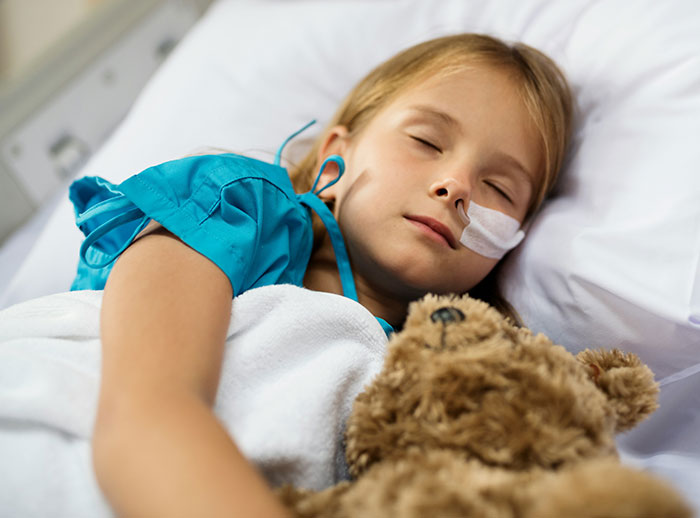 Child in hospital bed with teddy bear, theme of insurance claims being denied by UnitedHealthcare CEO.