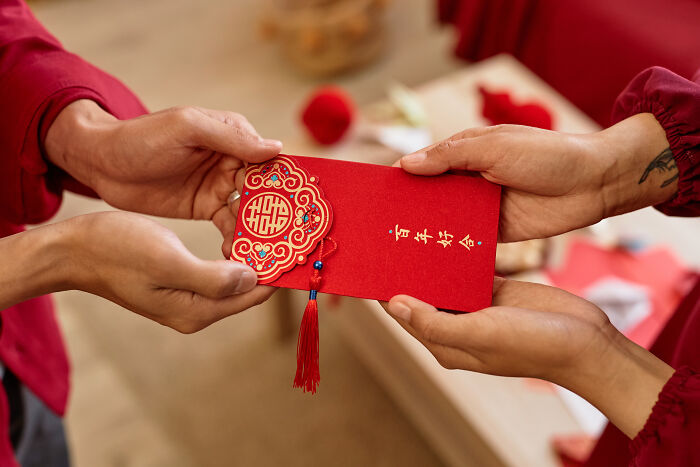 Hands exchanging a red envelope with intricate Chinese designs, symbolizing wealth and cultural tradition.