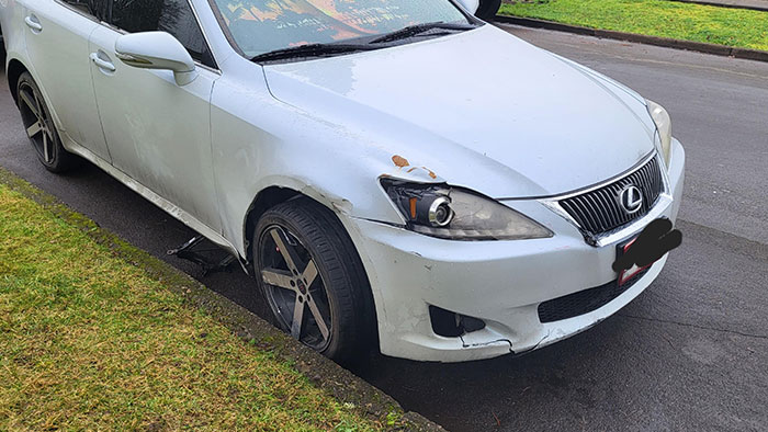 Damaged white car on street after Christmas accident, front bumper and wheel visibly affected.