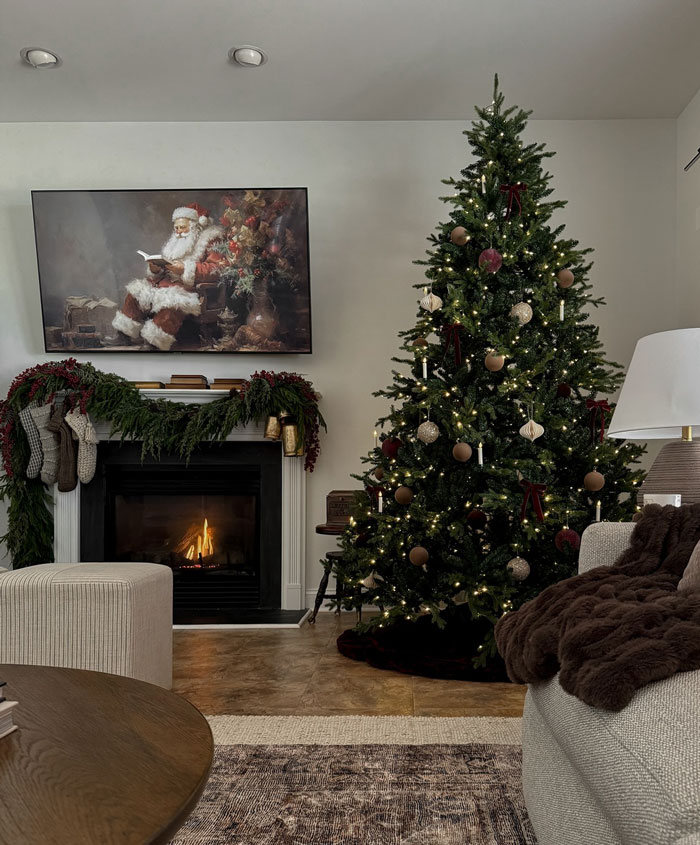 Christmas-decorating-ideas: Cozy living room with decorated Christmas tree, fireplace, and Santa painting above the mantel.