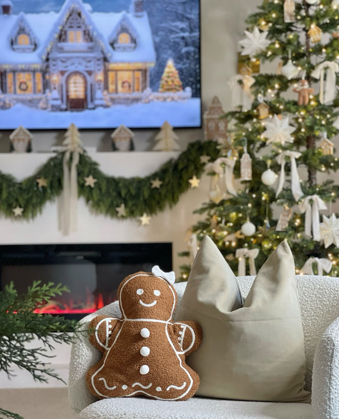 Cozy Christmas-decorating-ideas with gingerbread pillow, festive tree, garland, and holiday scene on TV above fireplace.