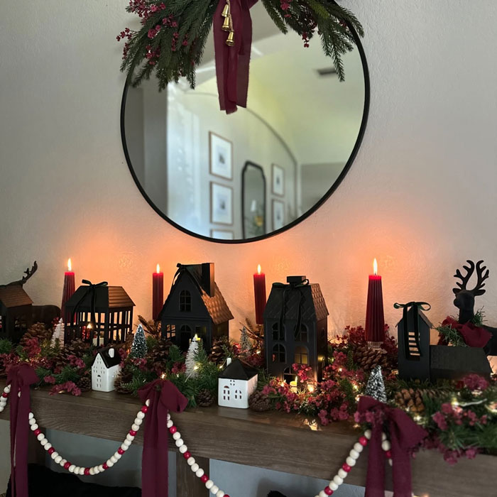 Festive mantel with candles, small houses, and greenery for Christmas decorating ideas.