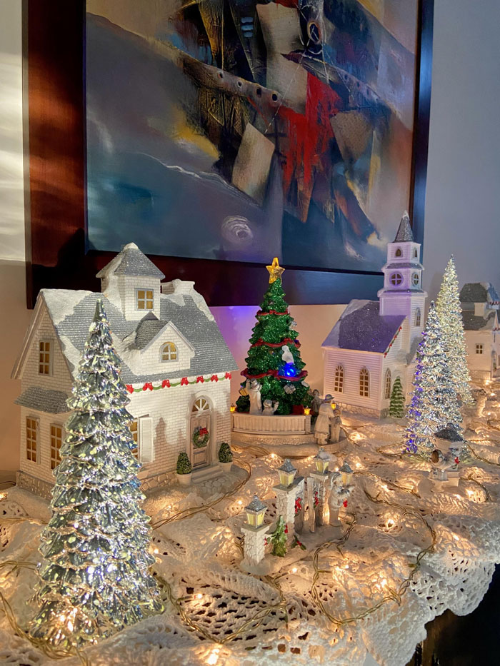 Miniature village with lit Christmas tree, surrounded by festive lights, showcasing Christmas decorating ideas.