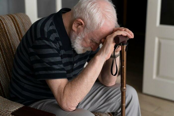 An elderly man seated with a cane, appearing contemplative, highlighting challenges of aging.