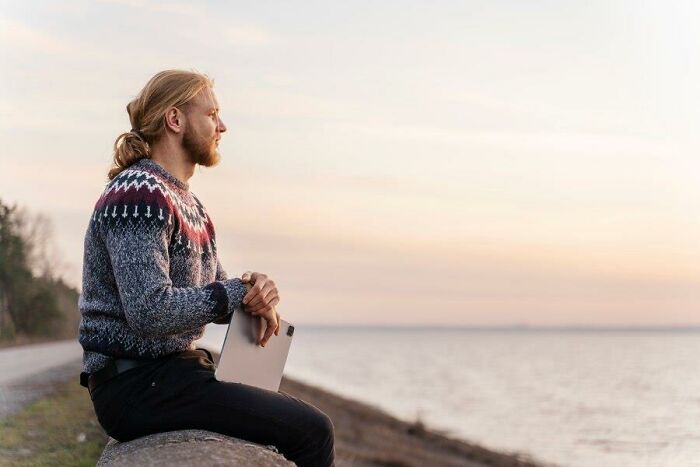 Man with tablet in hand, contemplating aging challenges by a serene seaside at sunset.