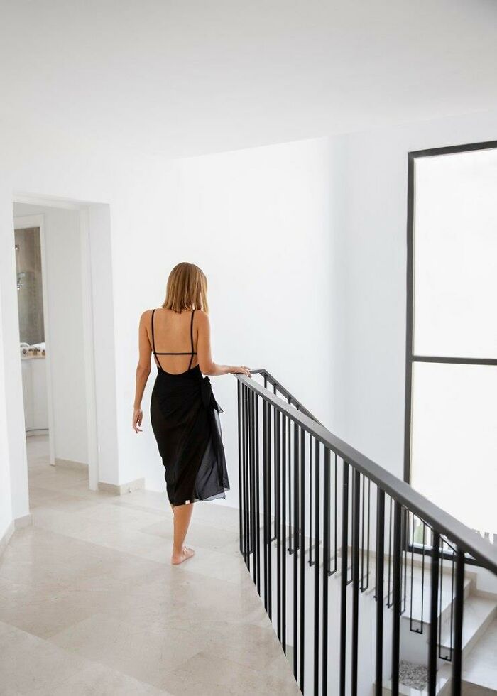 A woman in a black dress walks barefoot down a sunlit staircase, representing unexpected partner habits.