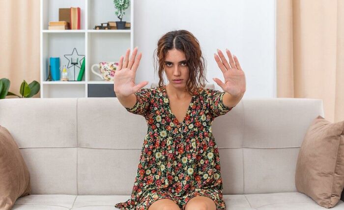 Person on a couch with hands raised, expressing surprise at partner's weird habits after moving in together.