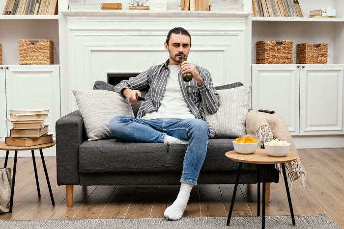 Man sitting on a couch, surrounded by snacks and books, highlighting partners' weird habits after moving in together.