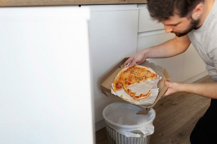 Man discovering a partner's weird habit of storing leftover pizza in a cardboard box above the trash can.