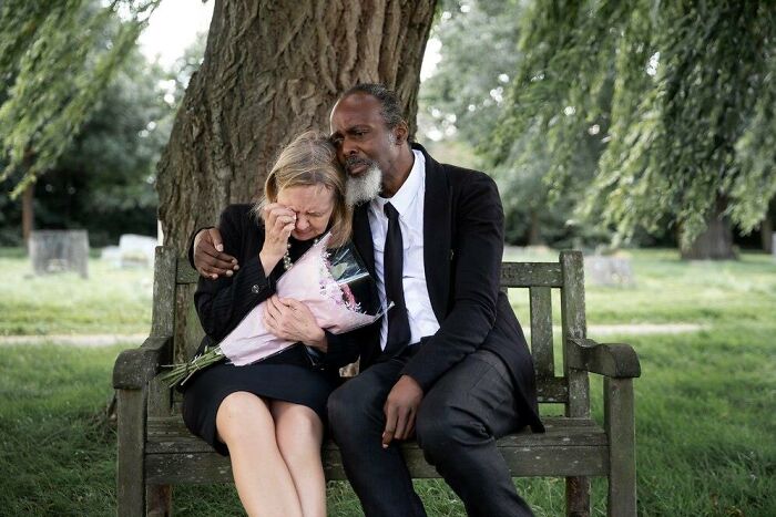 A man comforts a crying woman on a bench outdoors, both in formal attire, experience worst things happen wedding.