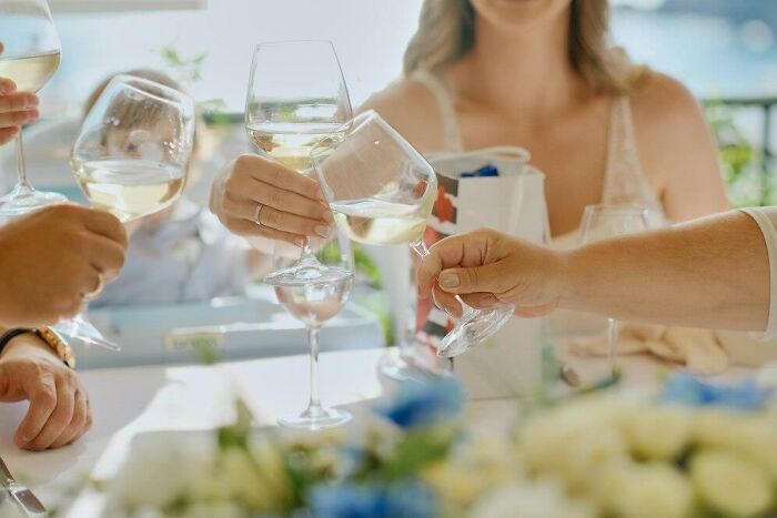 People clinking wine glasses at a wedding celebration under sunny skies.