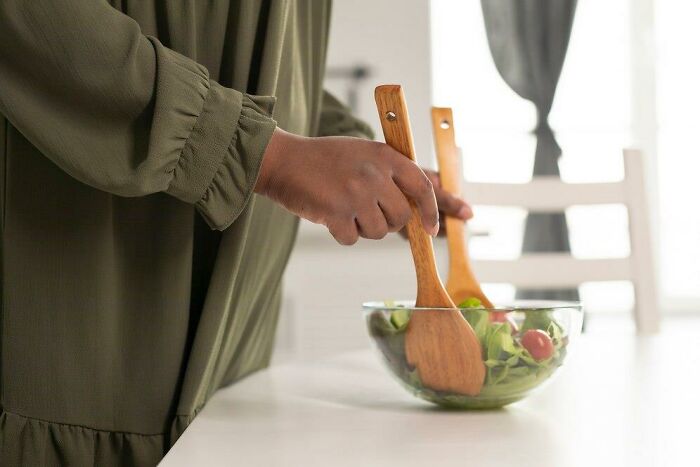 Person preparing salad with wooden utensils during a holiday meal preparation.