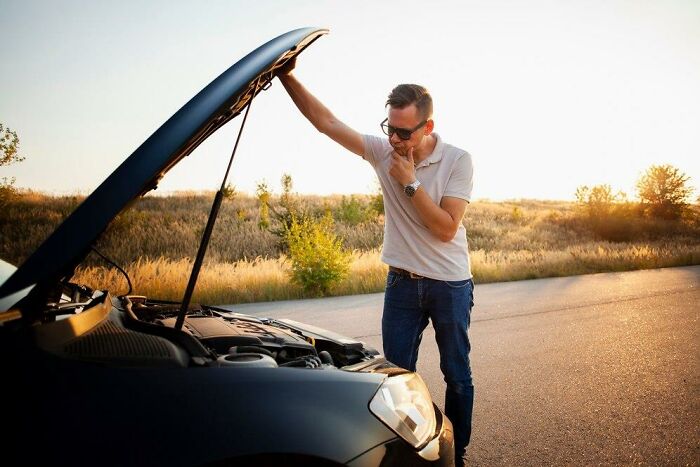 Man on a road with car hood open, appearing distressed during a terrible Christmas situation.