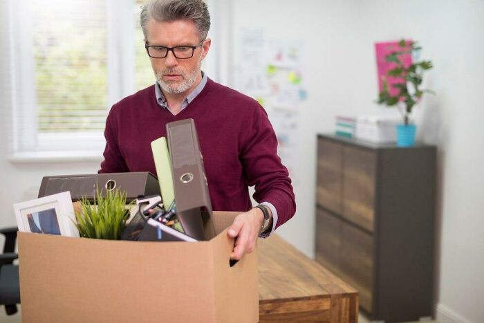 Man in an office, carrying a box with personal items, depicting a terrible Christmas experience.