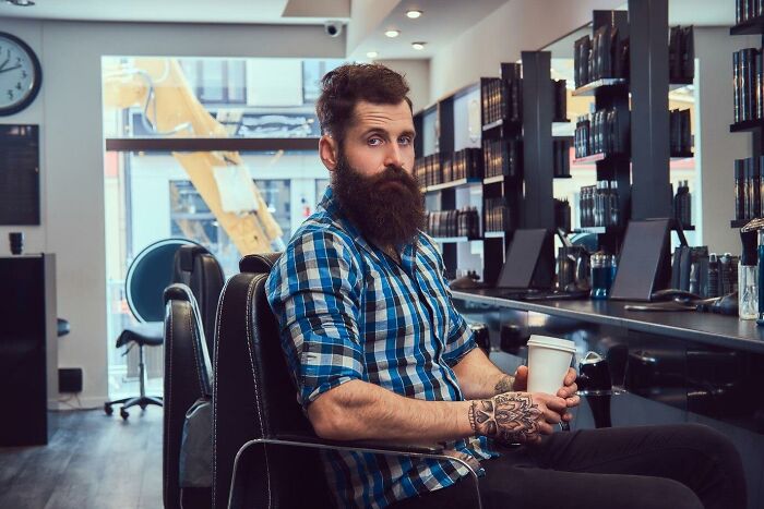 Man with beard in a barber shop holding a coffee cup, embodying "crazy stories" theme.