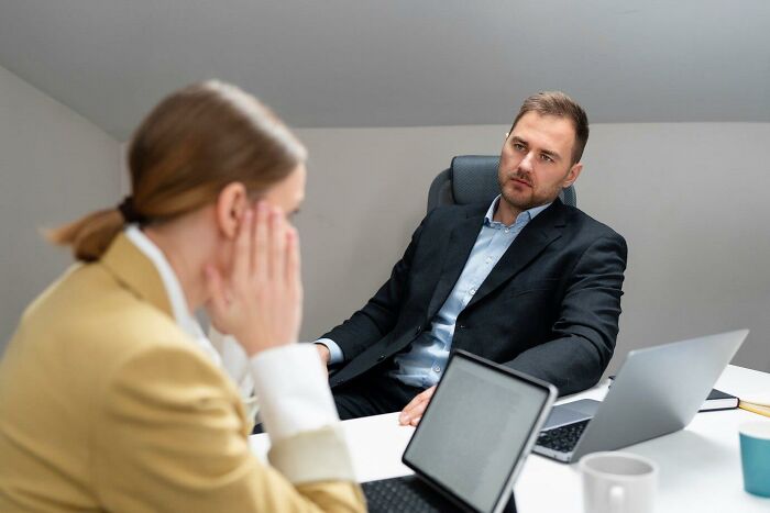 Two professionals in a meeting, discussing HR-related issues in an office setting with laptops on the table.