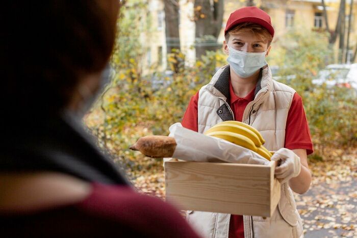 Delivery person wearing a mask and holding a box with bananas, showing the concept of HR not your friend.