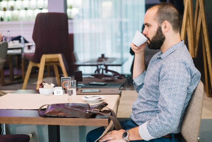 A man in a casual shirt sipping coffee at a café, illustrating a relaxed work-related conversation.