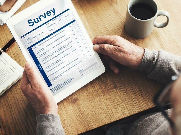 Person reviewing a survey on a tablet with a cup of coffee, relating to HR concerns and stories.