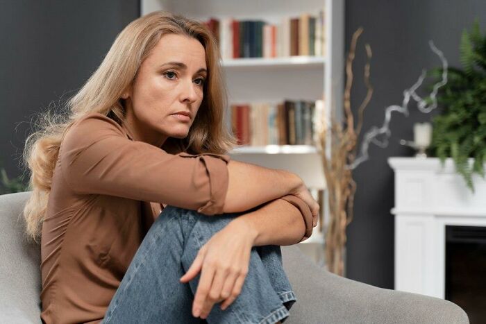 Woman sitting thoughtfully on a couch, surrounded by bookshelves, contemplating what's on a man's mind.