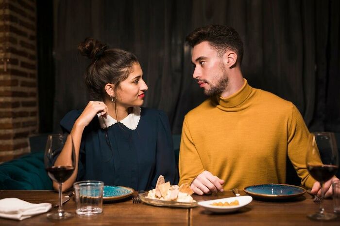 Man and woman at dinner table sharing a thoughtful moment, surrounded by wine and plates.